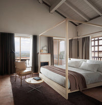 Luxury modern bedroom with canopy bed, natural materials, leather chair, and large windows