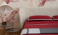 Luxury bed with red bedding, white upholstered headboard, parrot and butterfly wallpaper, modern lamp