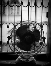 Vintage electric fan on a windowsill in front of iron bars, black and white photo