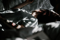 Person resting on a bed with soft natural light, showcasing luxury bedding comfort