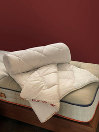 Luxury white duvet with quilted pattern displayed on a premium mattress against a red wall