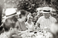Family enjoying outdoor meal together, smiling and sharing food at a garden table.