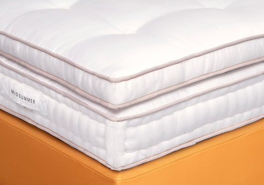 Close-up of a luxury white pillow-top mattress with quilted surface and orange bed base