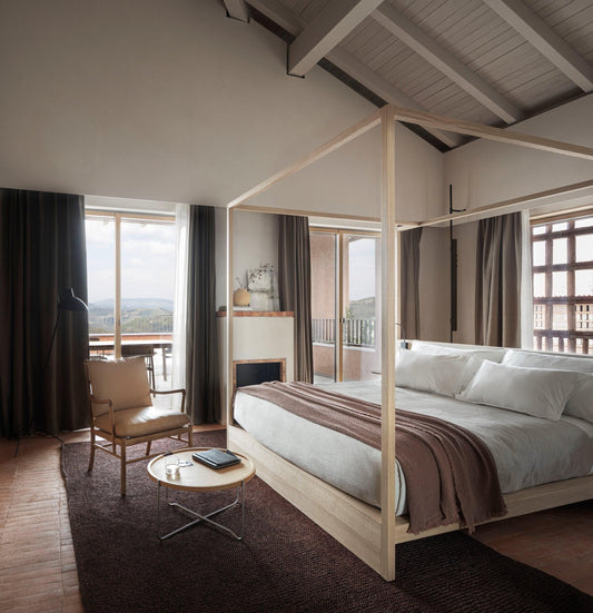 Luxury modern bedroom with canopy bed, natural materials, leather chair, and large windows