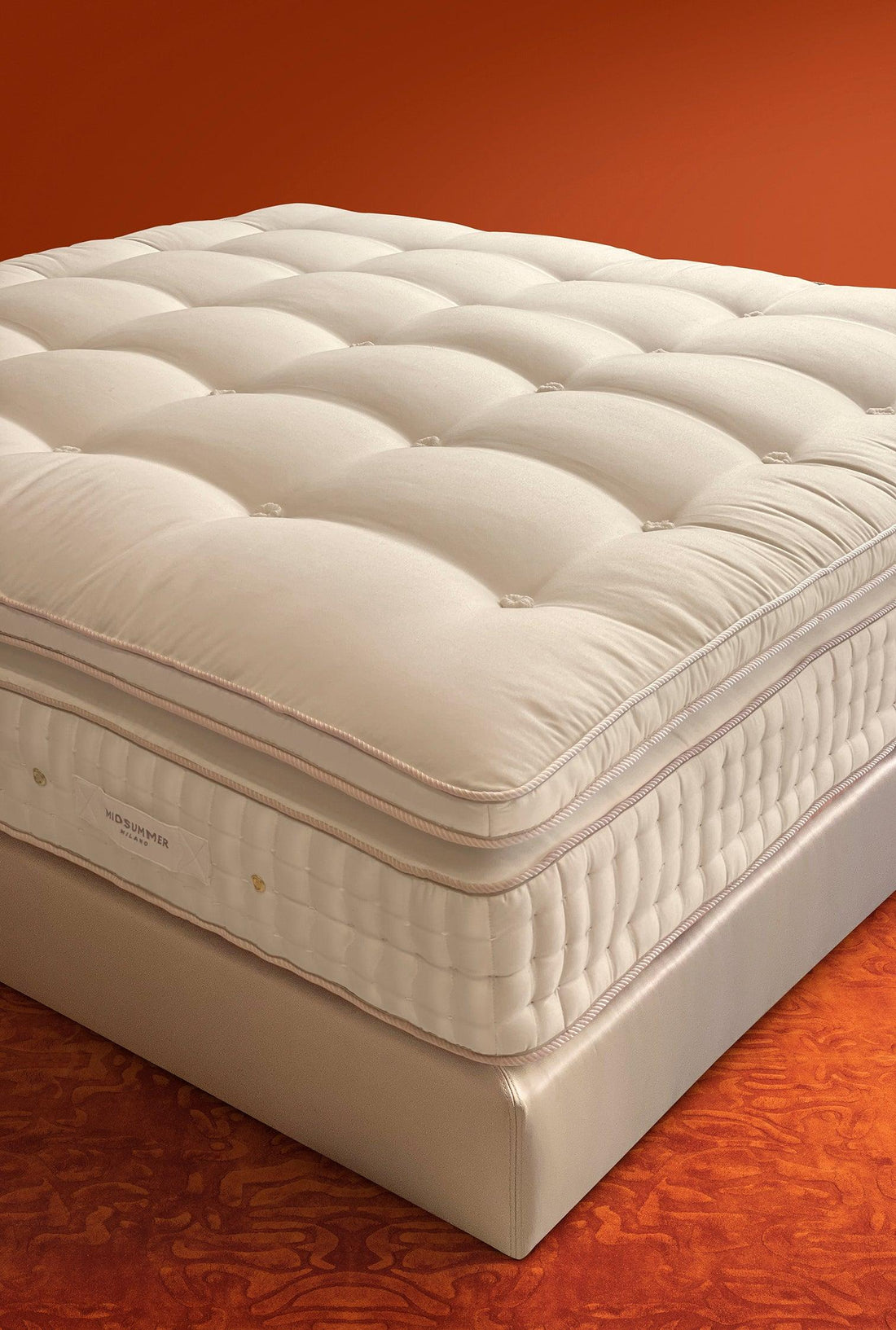 Luxury, tufted mattress topper on a premium bed base, soft texture, warm orange background.