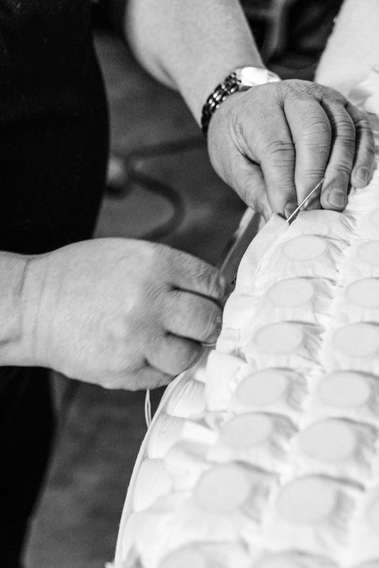 Artisan hand-stitching natural fabric on a luxury mattress in black and white close-up