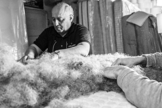 Artisan handcrafting a luxury mattress with natural fibers in a workshop setting