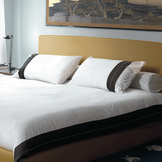 Luxury bed with beige headboard, white bedding, and elegant black trim pillows in modern room