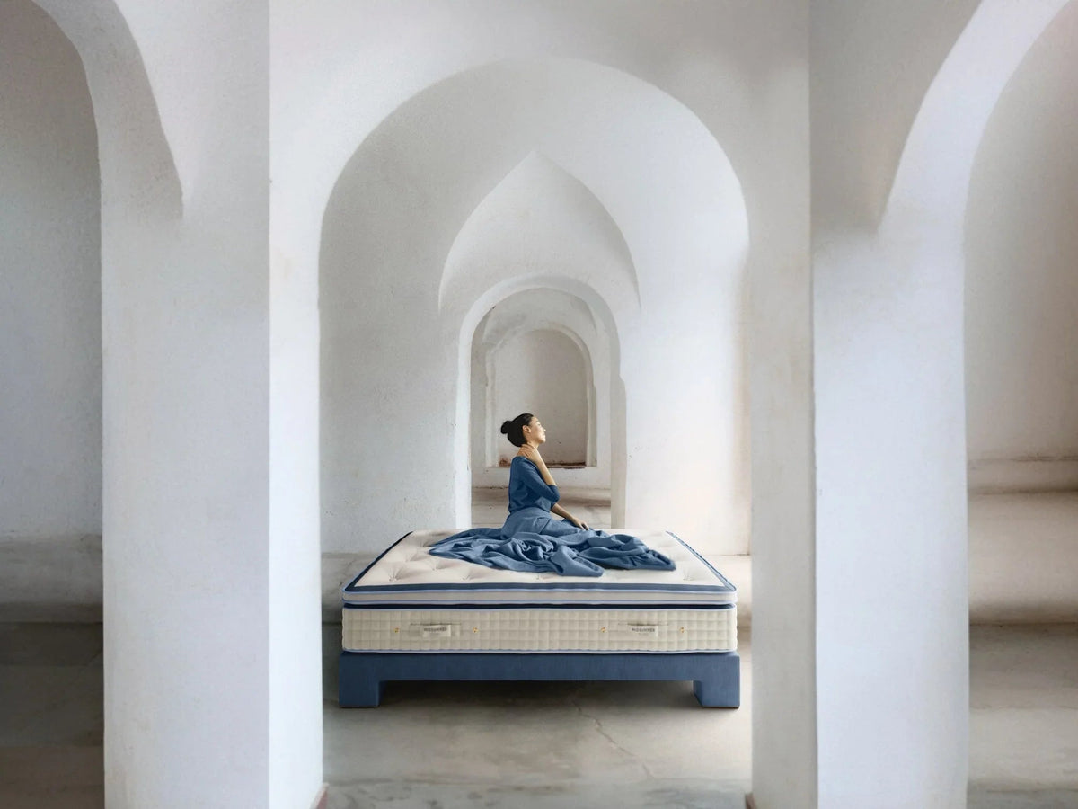 Woman sitting on luxury bed in modern arched room, elegant bedding and serene atmosphere