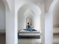 Woman sitting on luxury bed in modern arched room, elegant bedding and serene atmosphere