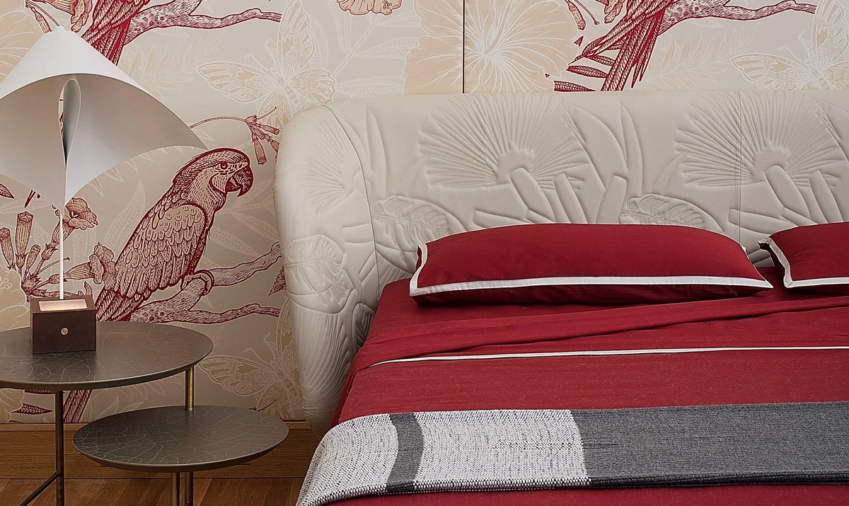 Luxury bed with red bedding, white upholstered headboard, parrot and butterfly wallpaper, modern lamp