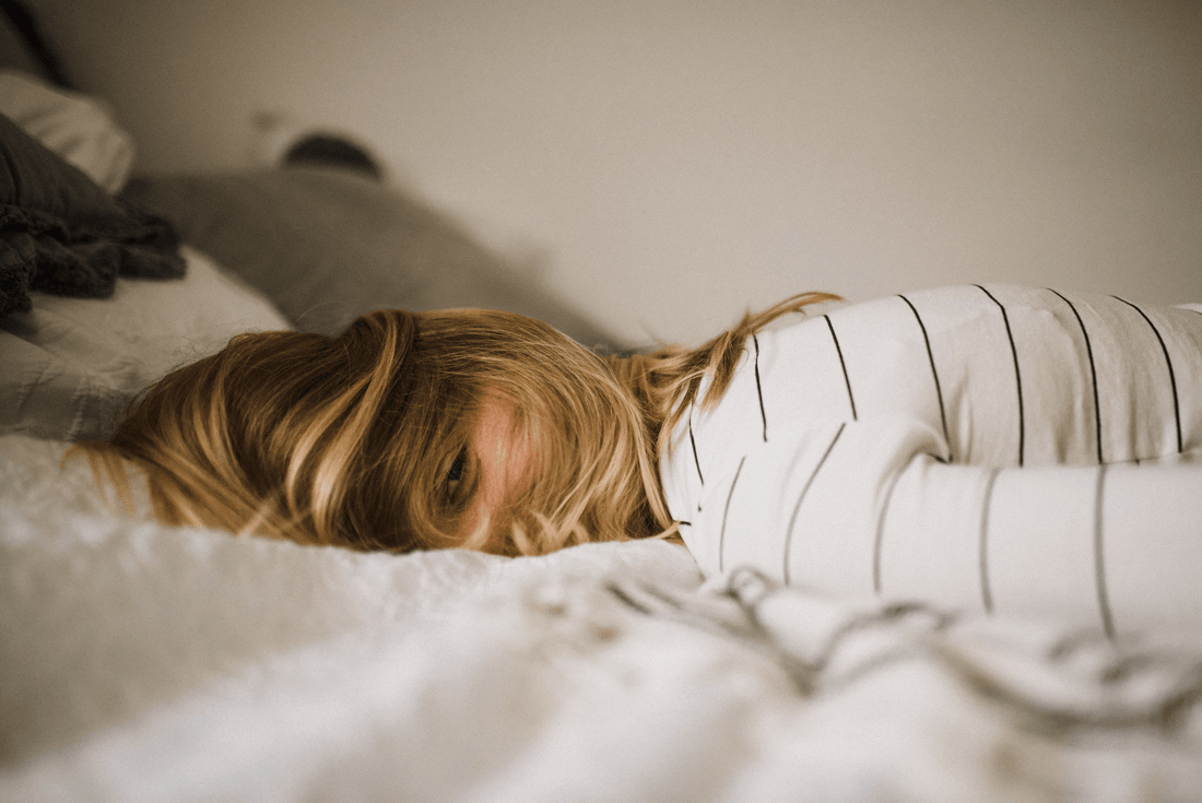 Woman with blonde hair in striped shirt lying face down on luxury bed