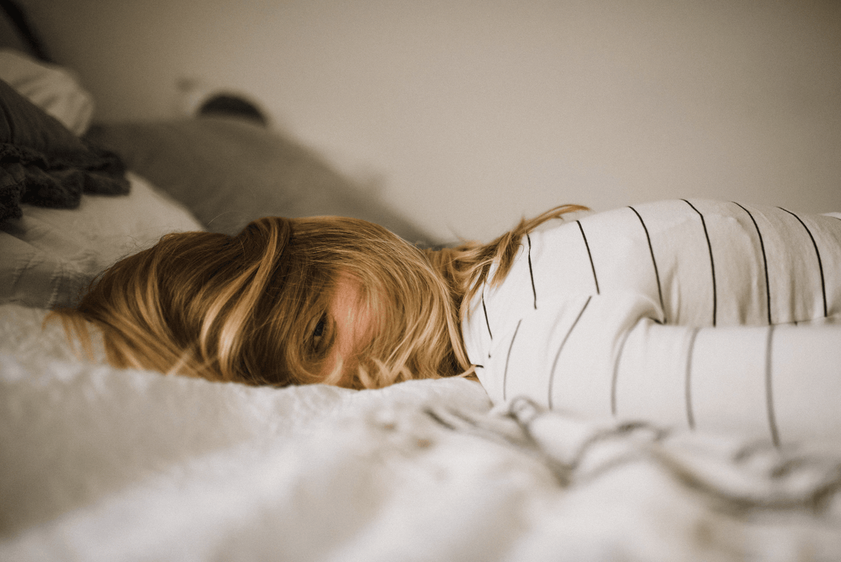 Woman with blonde hair in striped shirt lying face down on luxury bed