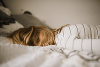Woman with blonde hair in striped shirt lying face down on luxury bed