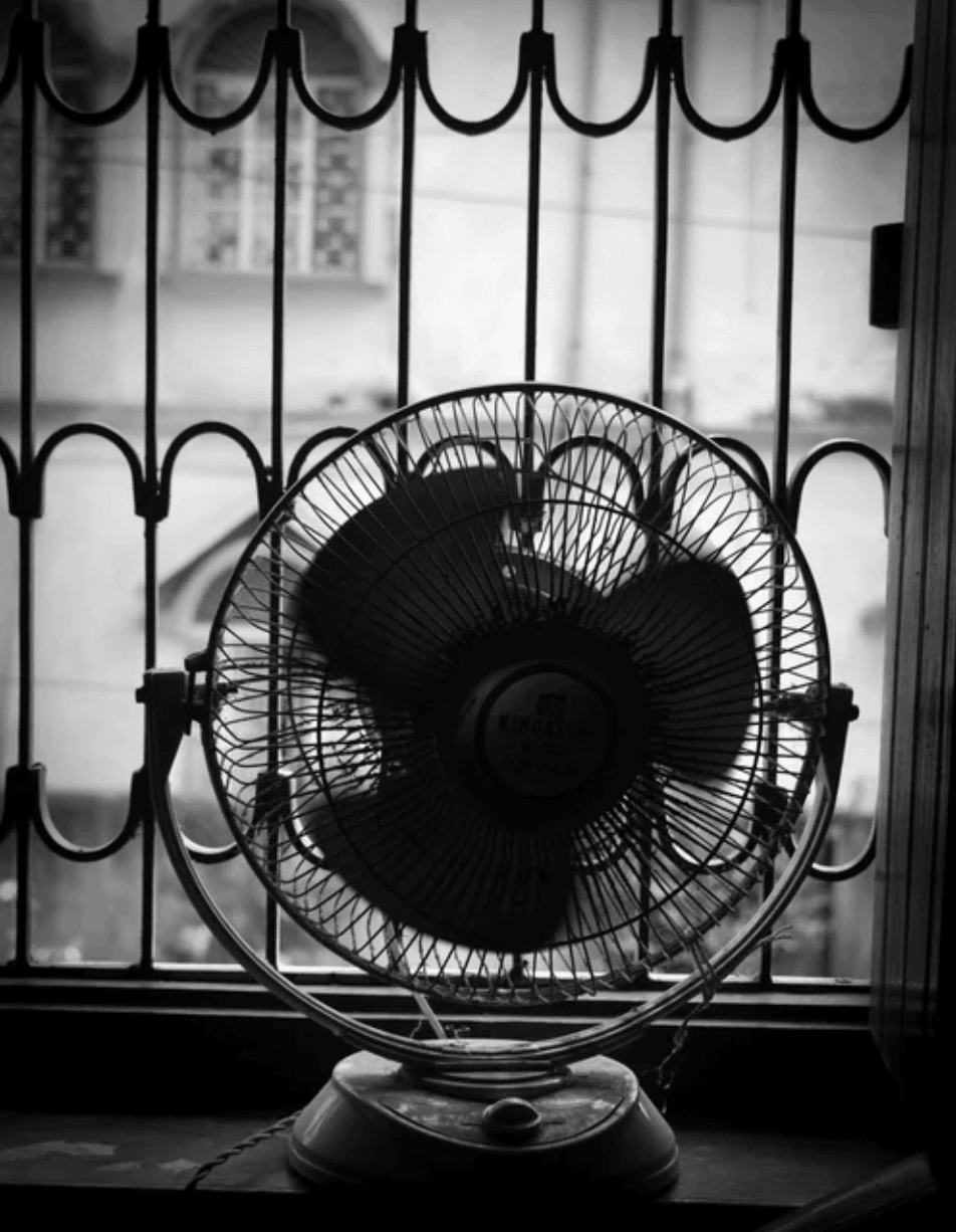 Vintage electric fan on a windowsill in front of iron bars, black and white photo