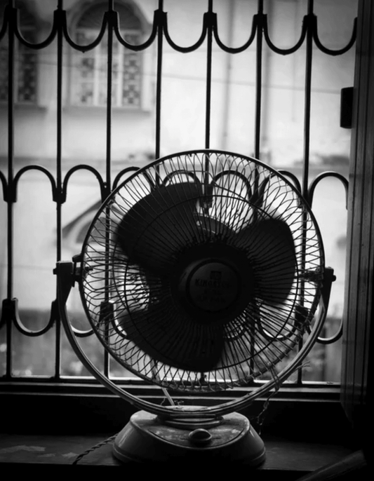 Vintage electric fan on a windowsill in front of iron bars, black and white photo