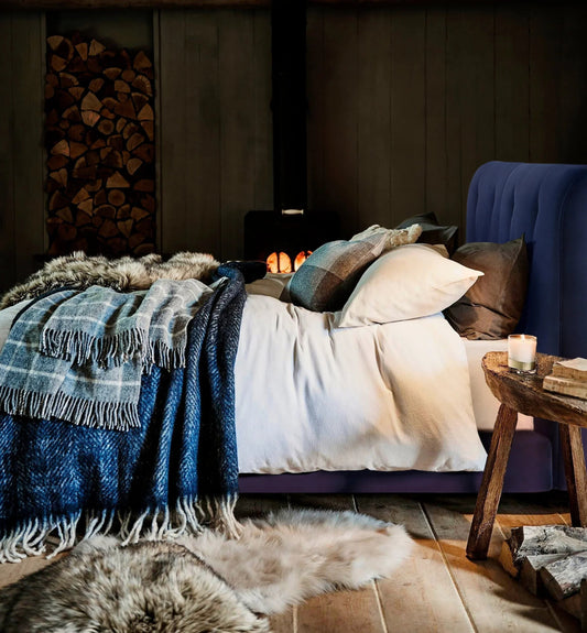 Luxury upholstered bed with cozy blankets and pillows in a rustic room with wood stove and fur rug