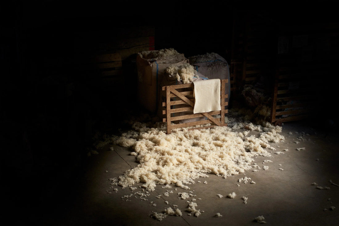 Natural wool fibers scattered on a concrete floor beside wooden crates in a dimly lit workshop