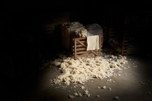 Natural wool fibers scattered on a concrete floor beside wooden crates in a dimly lit workshop