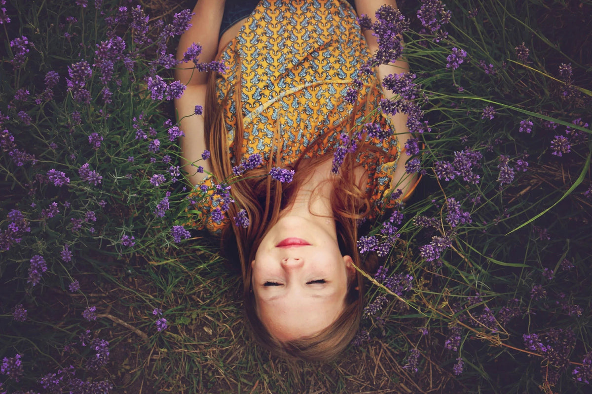 Woman lying in lavender field with relaxed expression, natural outdoor setting