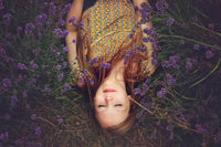 Woman in patterned dress lying in lavender field with eyes closed, surrounded by flowers
