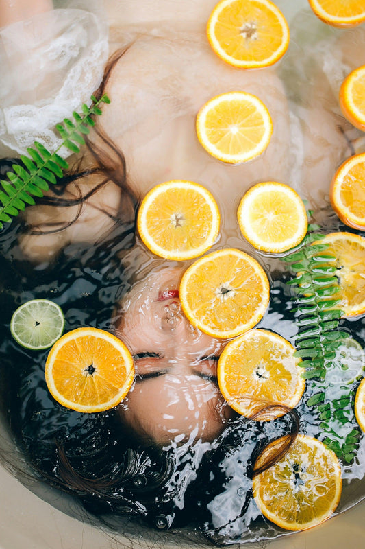 Woman relaxing in bath with orange slices, lime, and green fern leaves floating on water
