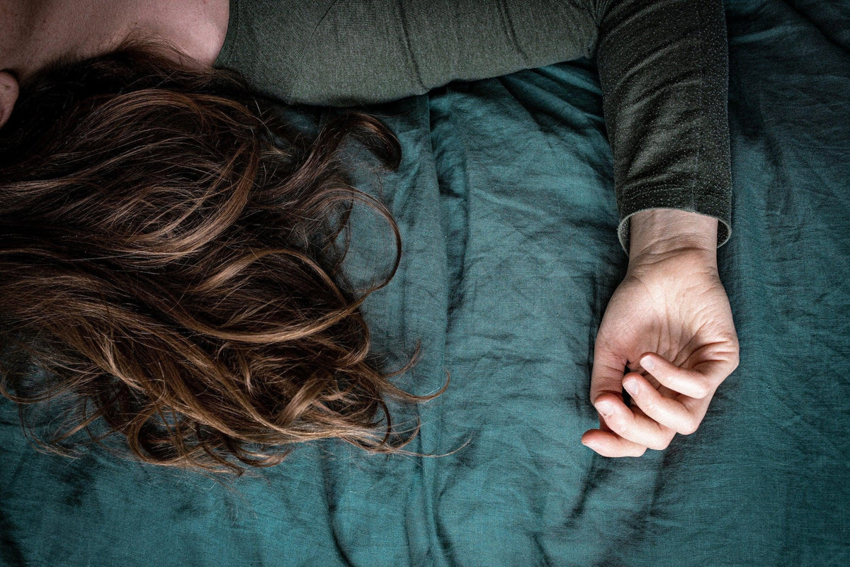Woman lying on a teal luxury bed, hand visible, focus on natural bedding fabric