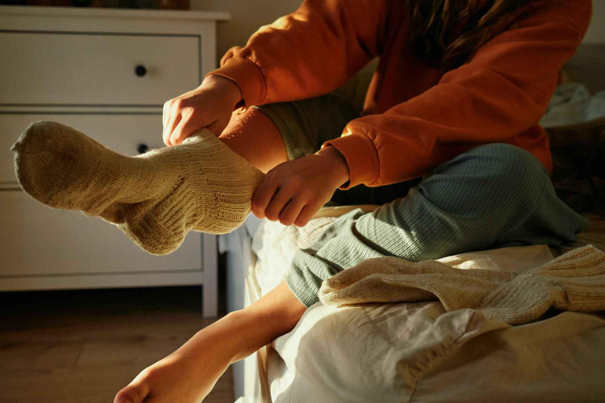 Person sitting on bed wearing cozy wool socks in morning sunlight, bedroom setting.