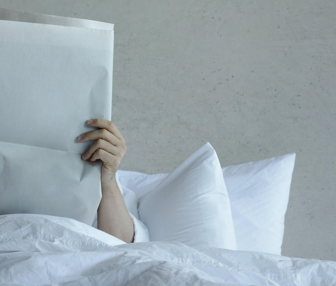 Person reading newspaper in bed with white luxury bedding and pillows