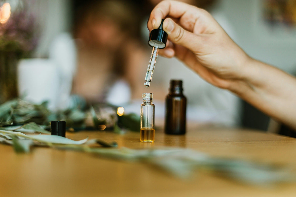 Hand using dropper with natural essential oil bottle, greenery on wooden table