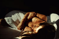 Woman relaxing on luxury bed with natural light, showcasing comfortable white bedding.