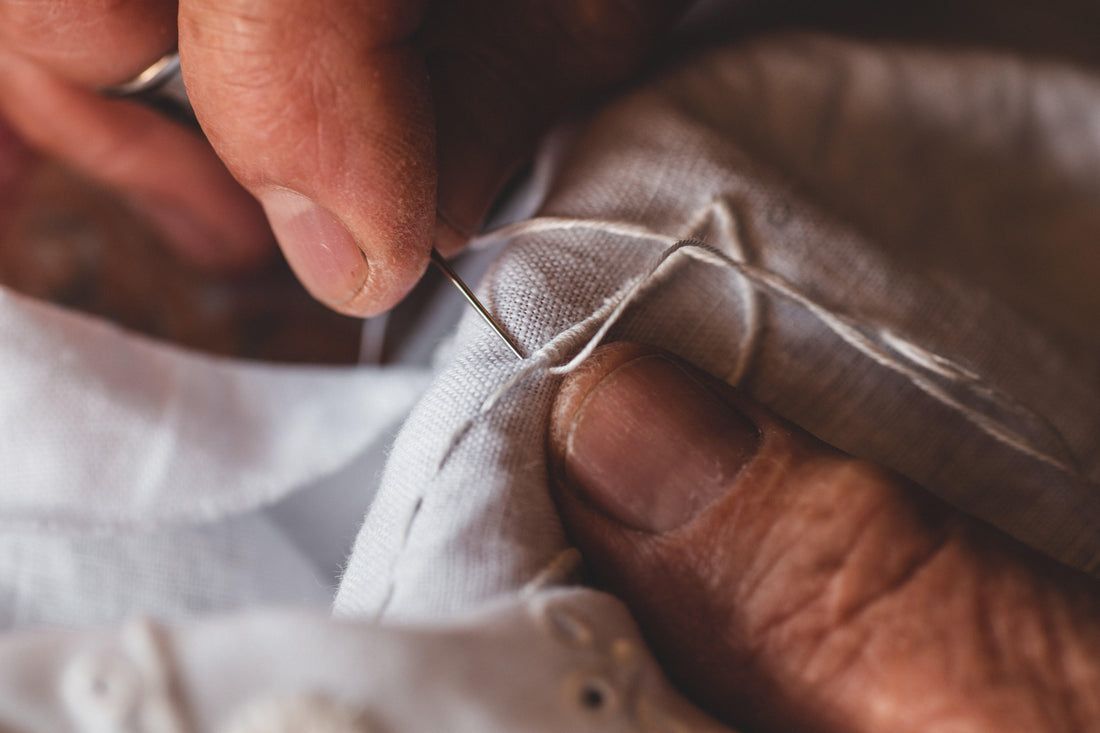 Close-up of hands hand-stitching fabric with needle and thread, artisanal craftsmanship detail