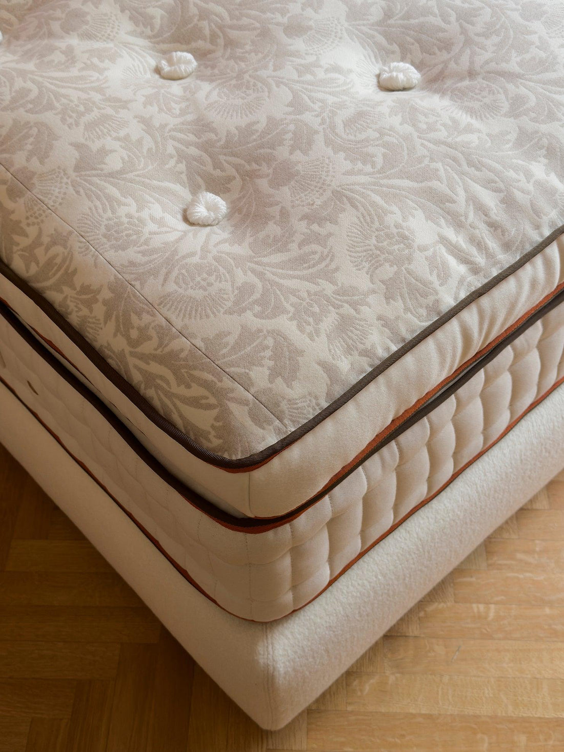 Close-up of a luxury tufted mattress with damask fabric and piped edges.
