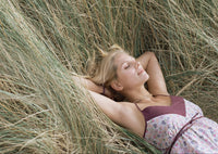 Woman relaxing in tall grass, enjoying nature and sunshine with a peaceful expression.