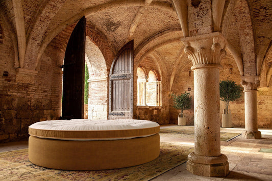 Round luxury bed with natural fabric in a historic stone vaulted room with rustic columns
