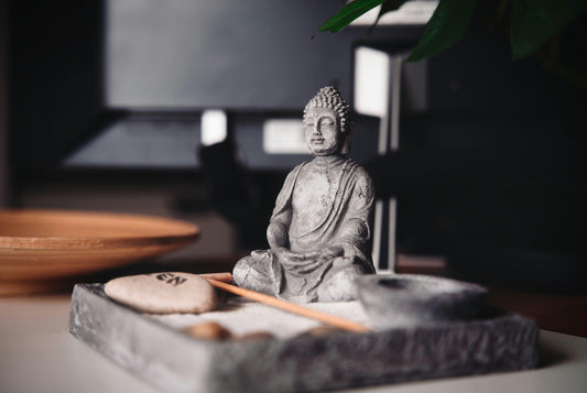 Grey Buddha statue and zen garden set with sand and stone on a modern indoor table