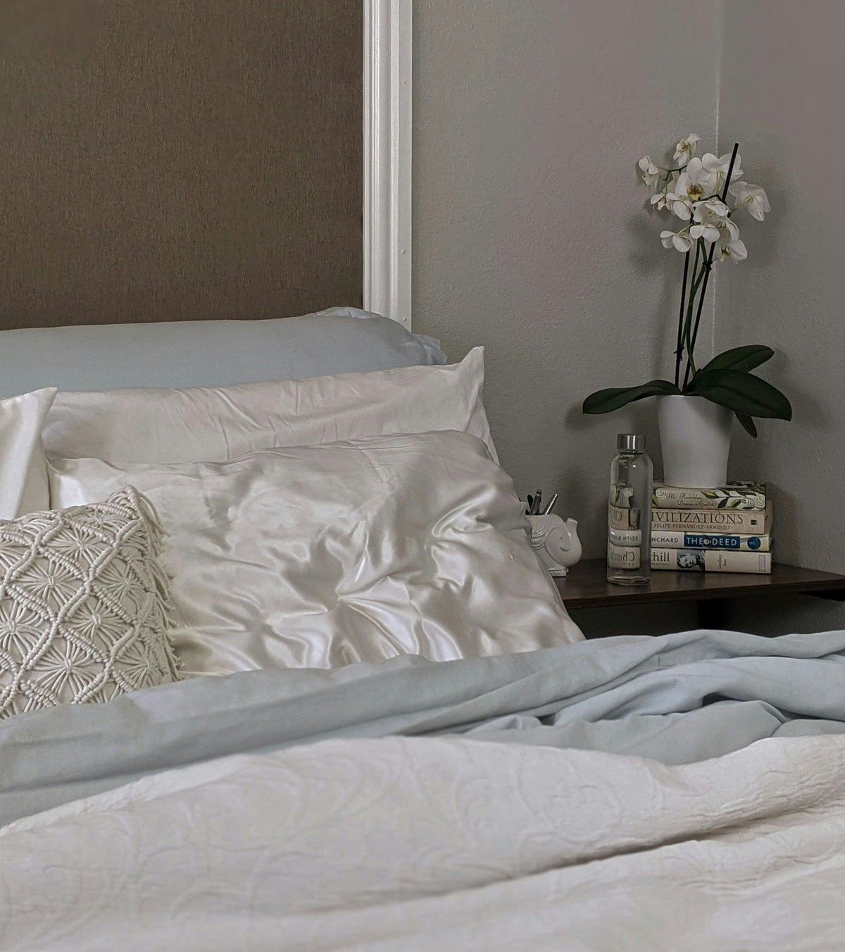 Luxurious bed with satin sheets, textured pillow, and modern nightstand with orchid and books