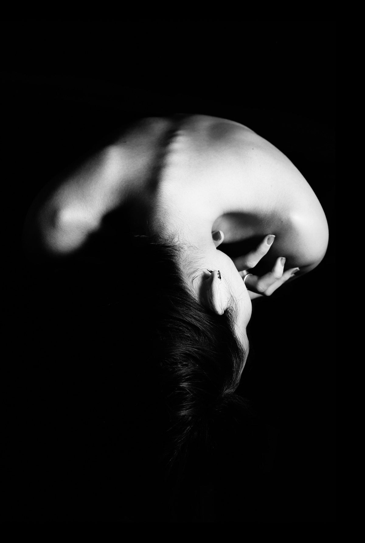 Artistic black and white photo of a person's bare back and shoulders in dramatic lighting