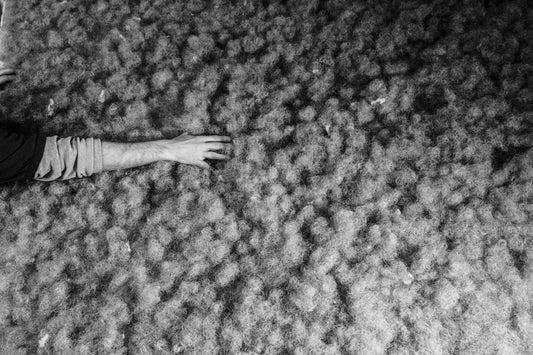 A hand touching a layer of raw, natural wool fibers for luxury mattress production.