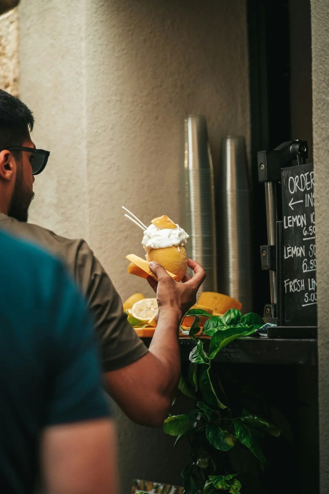 Man holding lemon sorbet dessert with whipped cream near a shop counter and menu sign