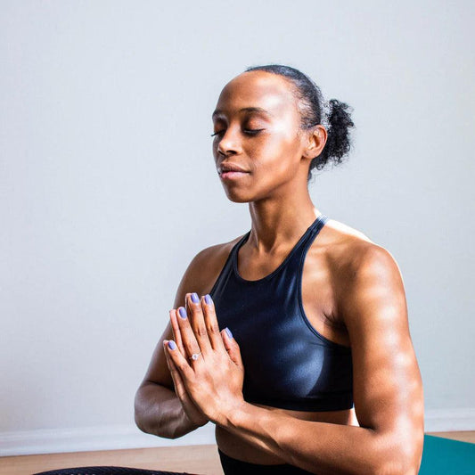 Woman practicing yoga meditation indoors, seated with hands in prayer position