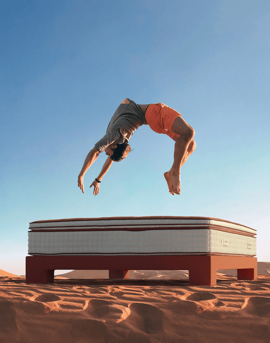Man doing a backflip above a luxury mattress on a modern bed frame in a desert landscape