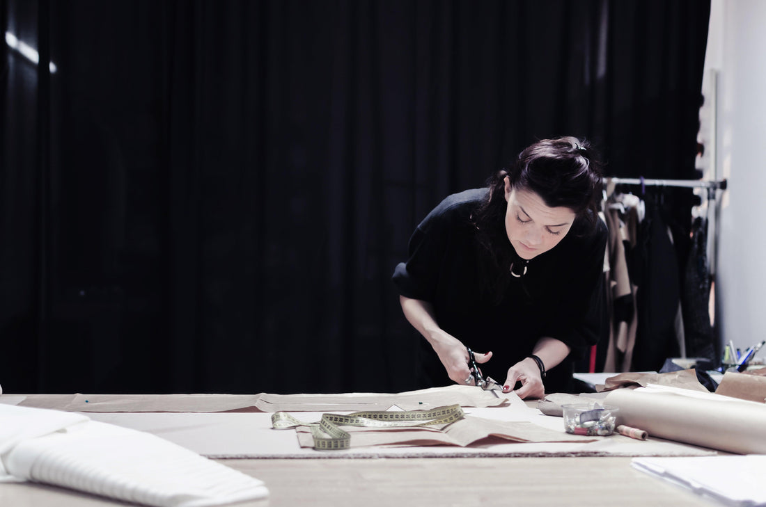 Artisan hand-cutting fabric with scissors on a worktable, tape measure nearby, in studio