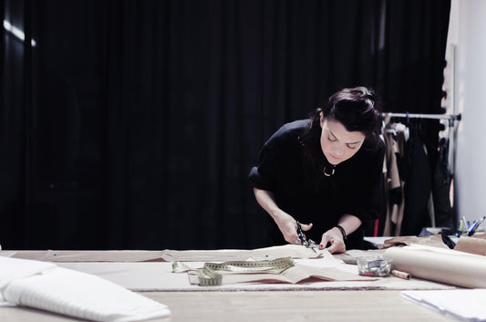 Artisan hand-cutting fabric with scissors on a worktable, tape measure nearby, in studio