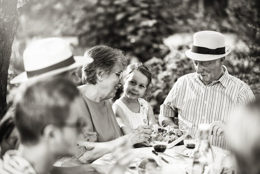 Family enjoying outdoor meal together, smiling and sharing food at a garden table.