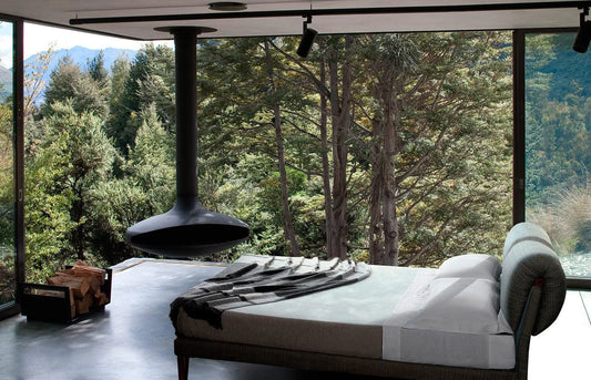 Luxury bed with blanket in modern room, large windows overlooking forest and mountains, hanging fireplace