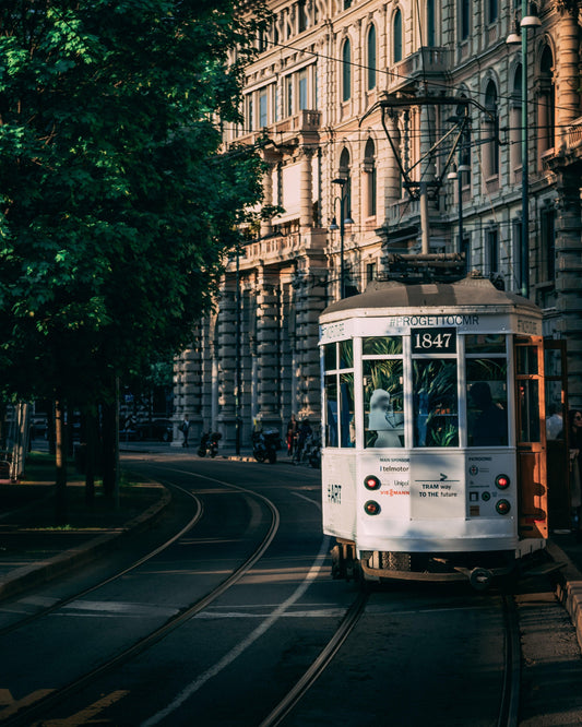 Historic white tram on curved tracks in Milan city with ornate Italian architecture