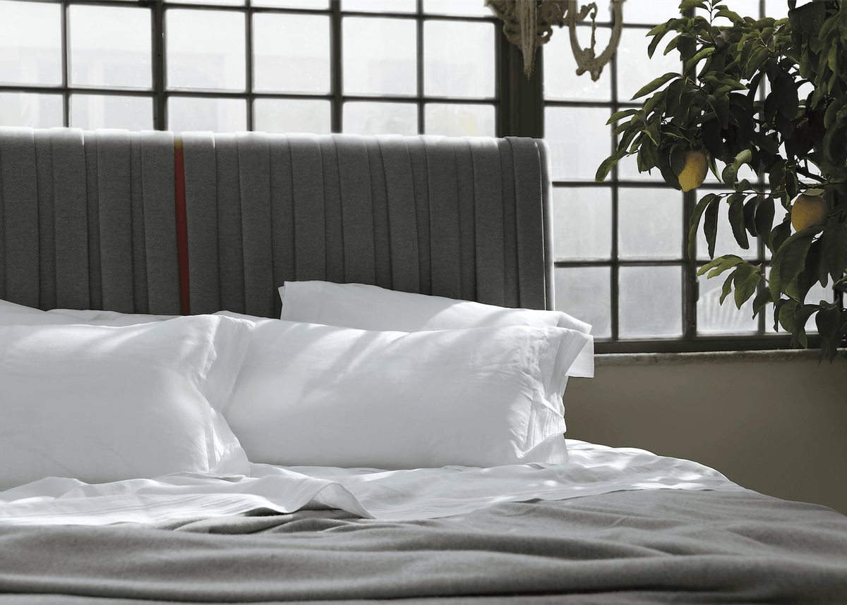 Luxury grey upholstered bed with white pillows, natural light, and a lemon tree nearby