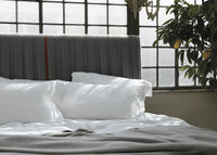 Luxury grey upholstered bed headboard with white linens and a lemon tree by the window