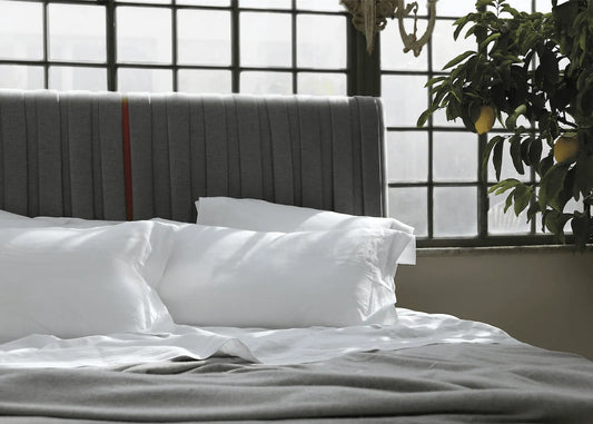 Luxury grey upholstered bed headboard with white linens and a lemon tree by the window